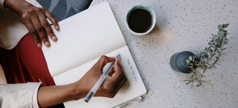 Person holding a white pen and paper while making a list on how to downsize your belongings before a move.