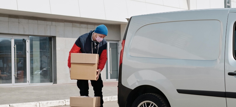 A man wearing a jacket is carrying boxes into a van.