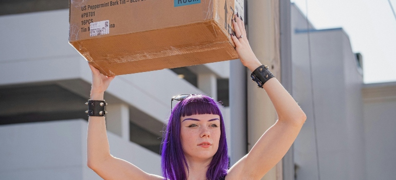 A woman holding up a box, thinking about tips for moving out for the first time.