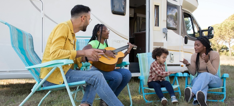 A family sitting near the campervan and singing with the guitar.
